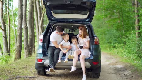 travel by car happy young family trip together vacation. parents dad and mom with cute children near sitting in the car trunk at camping