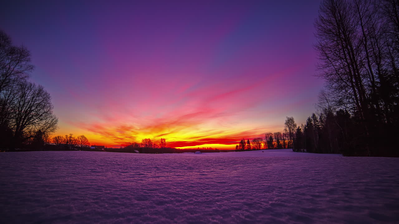 timelapse de nubes moviéndose en un cielo colorido con sol naciente en el horizonte sobre un paisaje nevado al amanecer