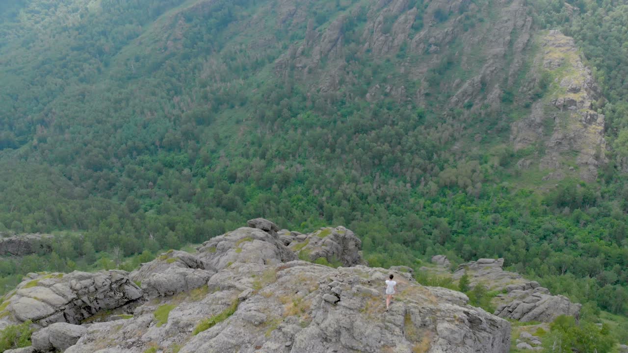 drone vuela sobre montañas impresionantes con una chica caminando en un acantilado