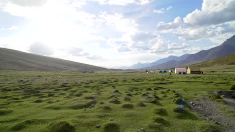 handheld shot as walking around a tent camp in the mountains on a sunny day, on an open green field with grass