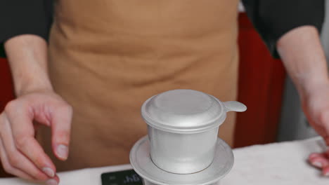 close-up of a barista's hand placing the metal cover on a coffee phin