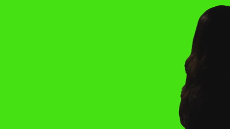 silhouette of woman walking across frame talking on mobile phone against green screen background with low key lighting 1