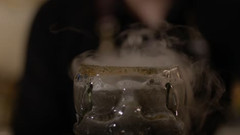 el cóctel se vierte cuidadosamente en un vaso en forma de calavera, con capas coloridas de ingredientes que crean una presentación visualmente llamativa e intrigante