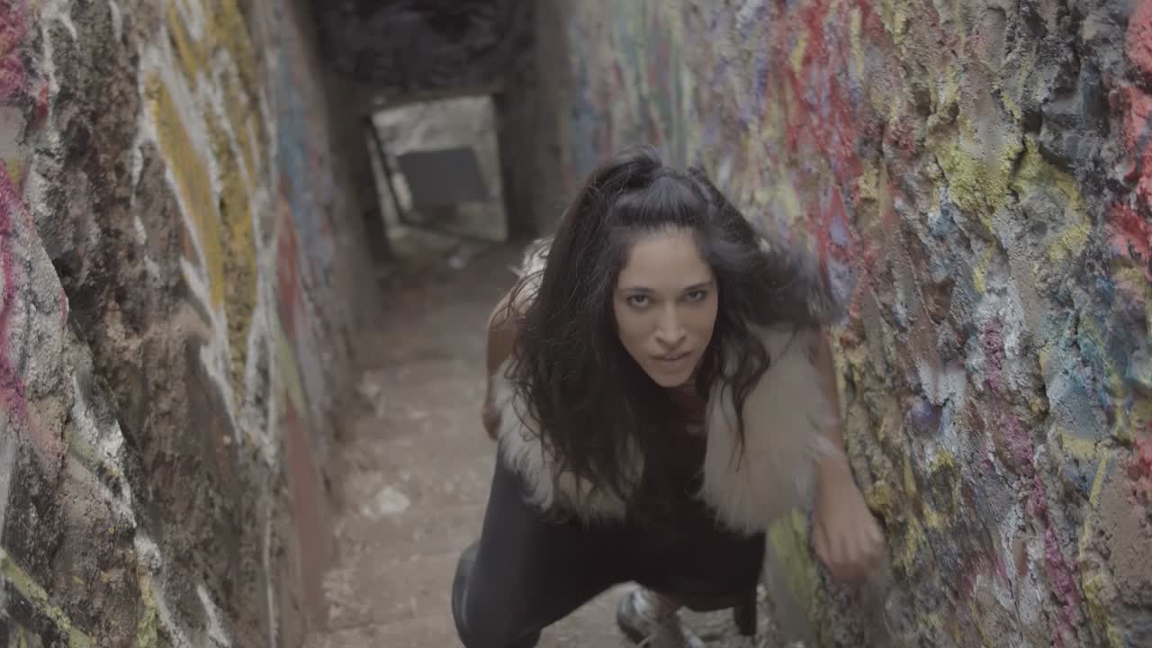 A woman trapped in a colorful abandon staircase squares off with the camera in a primal interpretive dance