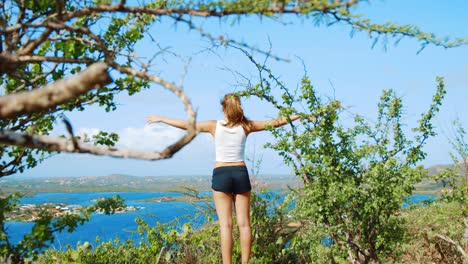 girl with arms outstretched up high with view of caribbean bay