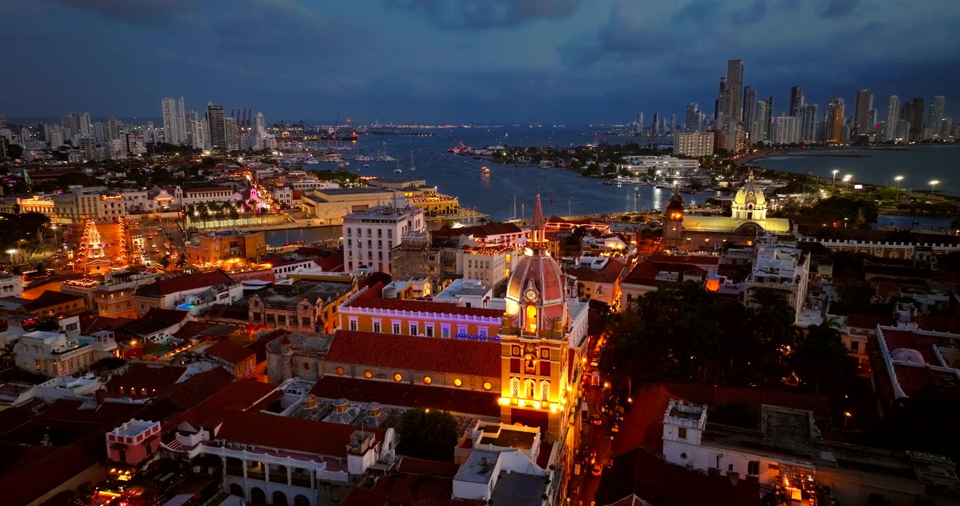 Inclinação de drone ao crepúsculo revela a catedral iluminada de Cartagena e Bocagrande ao fundo.