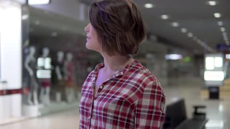 young beautiful brunette woman in a shirt walking in the shopping mall near the shops