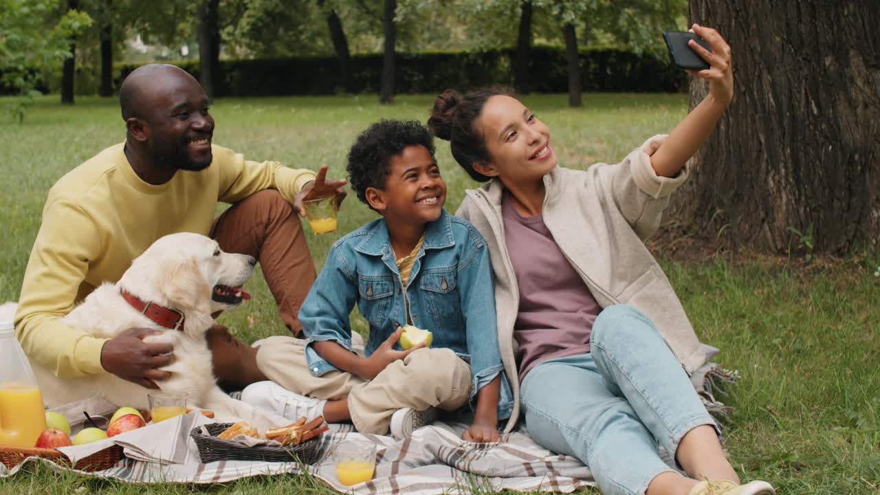 Positiv afroamerikansk familie tar en selfie med telefon på piknik