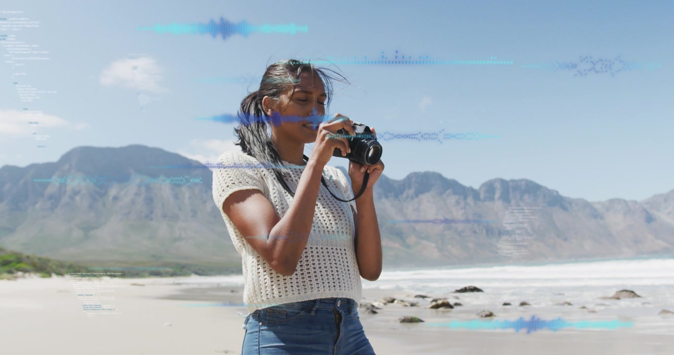 Photographer raising DSLR and composing coast shots on shore, checking lens, blue overlays guiding
