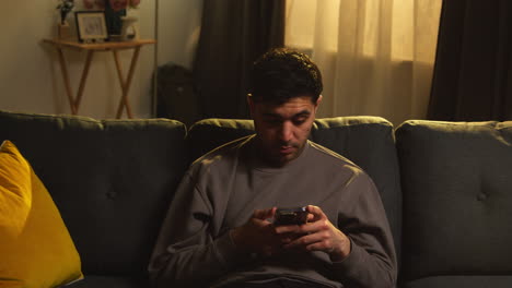 young man spending evening at home sitting on sofa with mobile phone scrolling through internet or social media 5