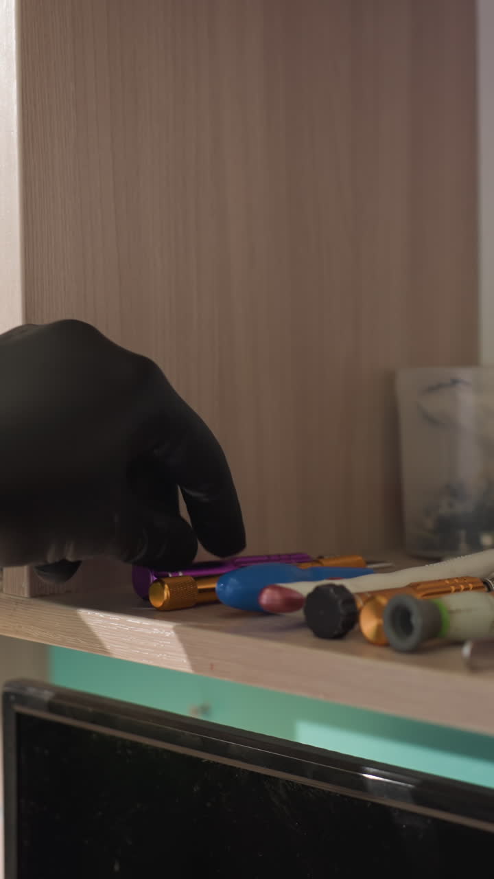 una vista de cerca de varias herramientas de laboratorio ordenadamente dispuestas en un estante, con una mano con guante seleccionando un artículo en el estante