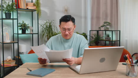 stressed asian man looking at unpaid bank debt loan, doing paperwork planning budget throws bills