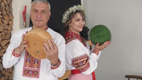 portrait of a beautiful older woman and man in embroidered authentic ukrainian attire with flowers in her hair, holding large round pieces of cheese wheels