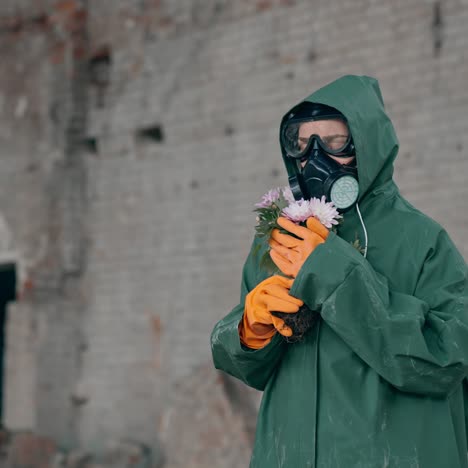 nature in danger. ecologist in safety suit and gas mask holding broken flowers in abandoned place. biochemical attack. polluted environment