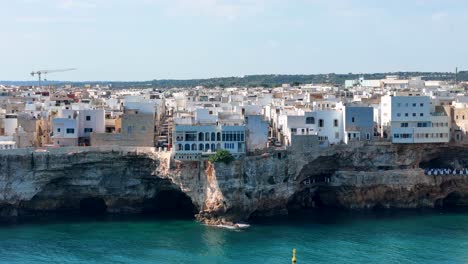 revelación aérea lenta de polignano a mare: calles pintorescas, acantilados dramáticos, aguas turquesas, italia