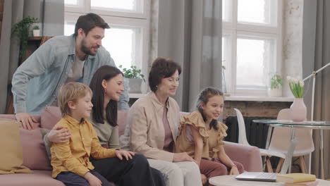 a family is sitting on a sofa watching a video call on their laptop