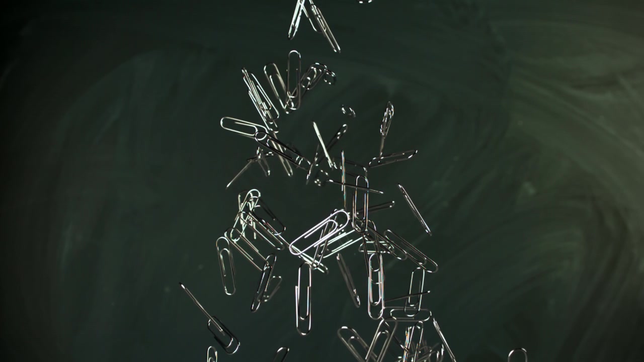 Paper Clips Floating and Scattering Against a Dark Background in Slow Motion