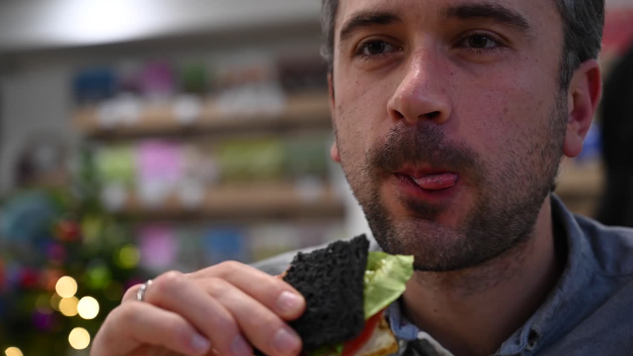 Close up of a man eating a burger with black buns