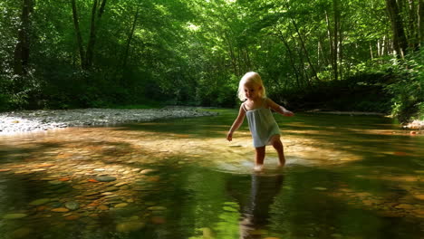 little girl wading in a sunny forest stream