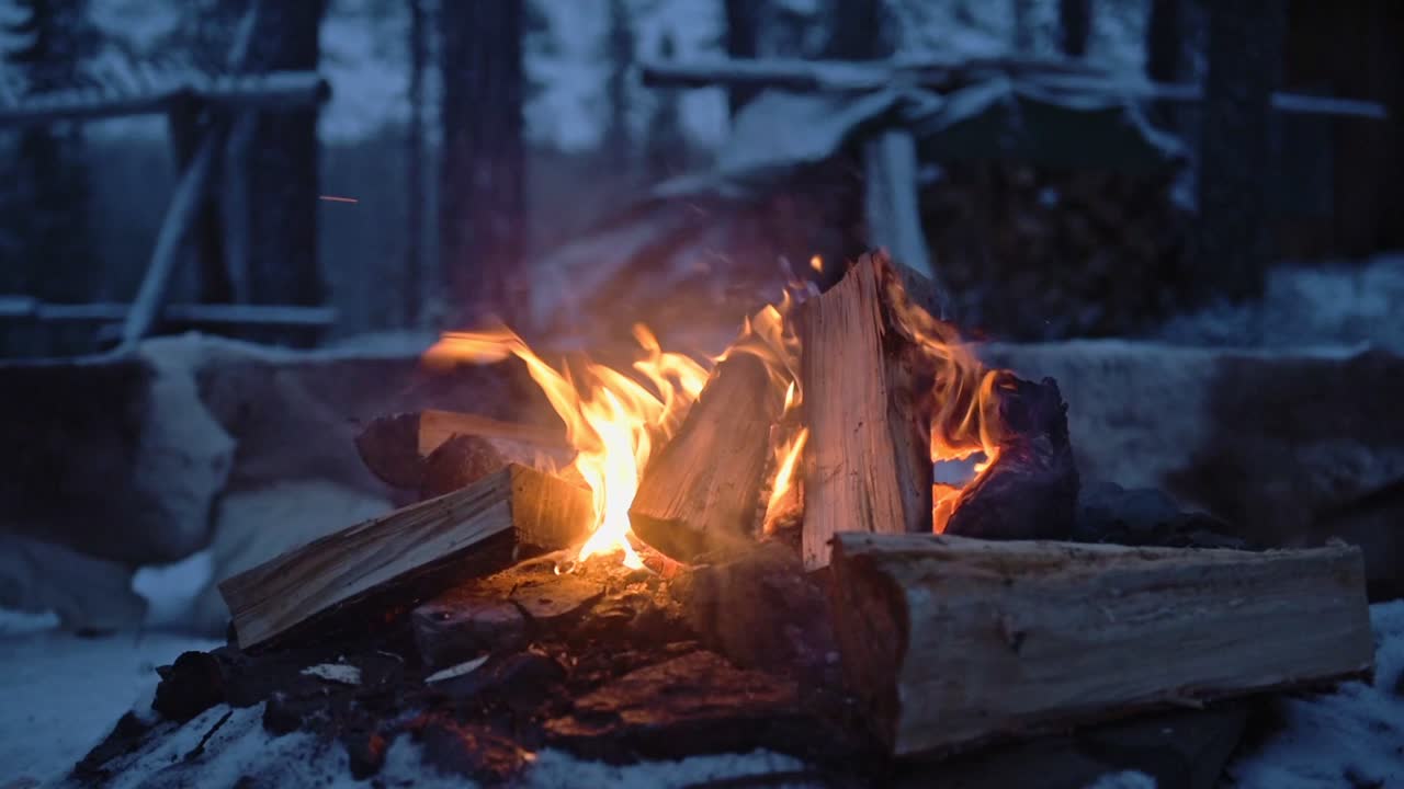 Logs burning in a outdoor campfire, surrounded by snow, on a windy evening in Lapland, Finland