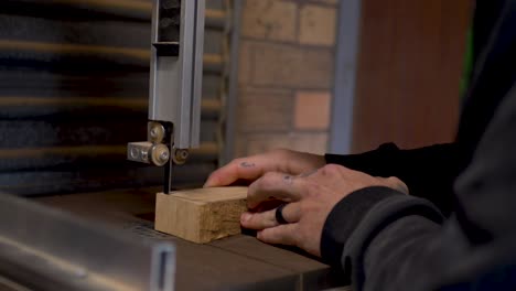 Slow motion close-up of man with ring cutting timber hardwood block on with electric bandsaw blade machinery power tool on bench at garage shed workshop for indoor climbing in Australia DIY project