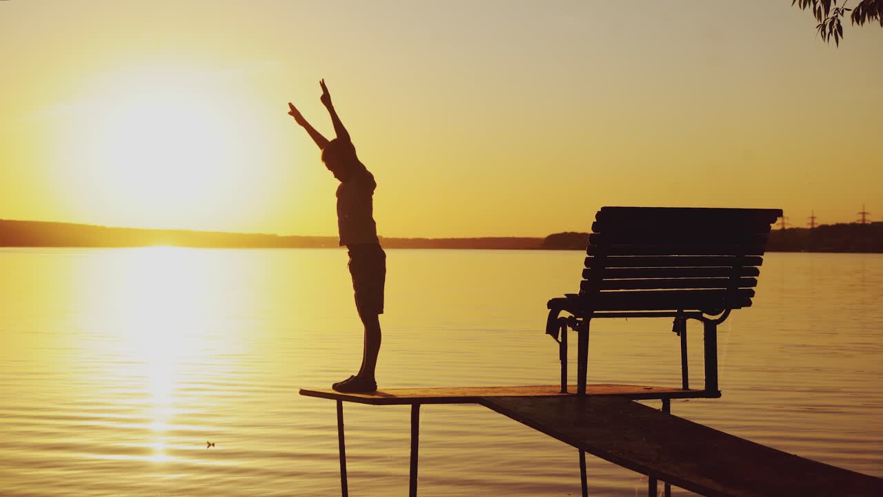 boy are doing physical activities on the bridge near the bench on the background of sunset by the river