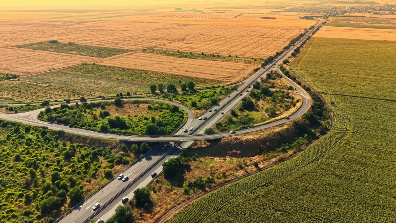 El tráfico fluye por una autopista con campos y tierras de cultivo a los lados al atardecer.