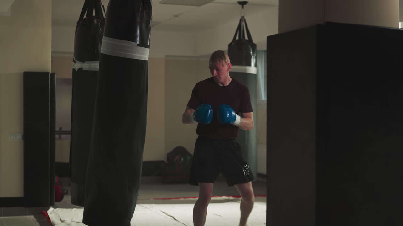 Man trains kick techniques on punching bag in gym. Professional kick-boxer trains with heavy equipment in sports club slow motion. Aggressive workout