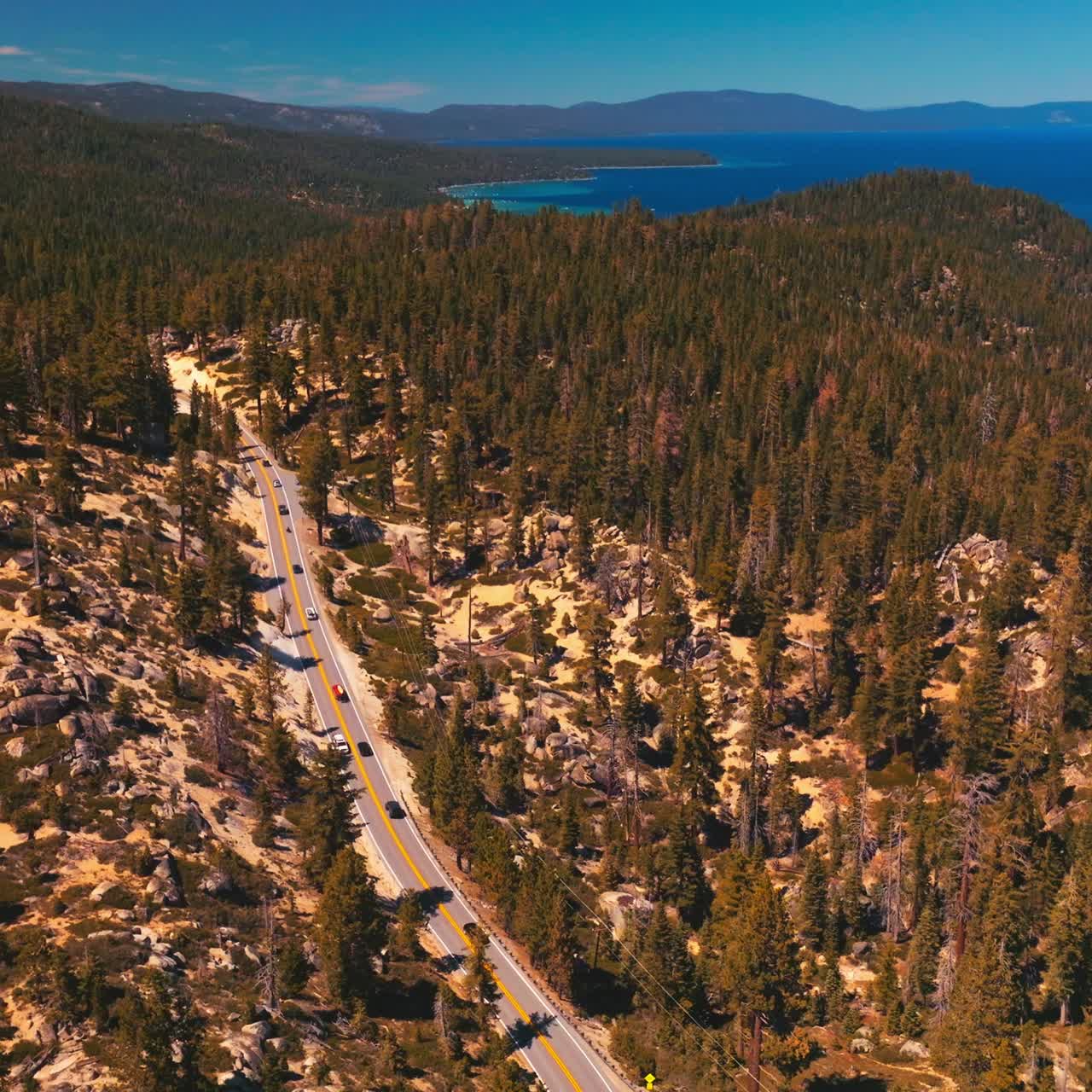 Rising over the mountainous landscape covered with pine tree forest. Road through the wood in the rocks. Blue lake at the foot of mountains