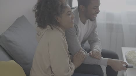 joven pareja afroamericana riéndose mientras ve un programa en la televisión