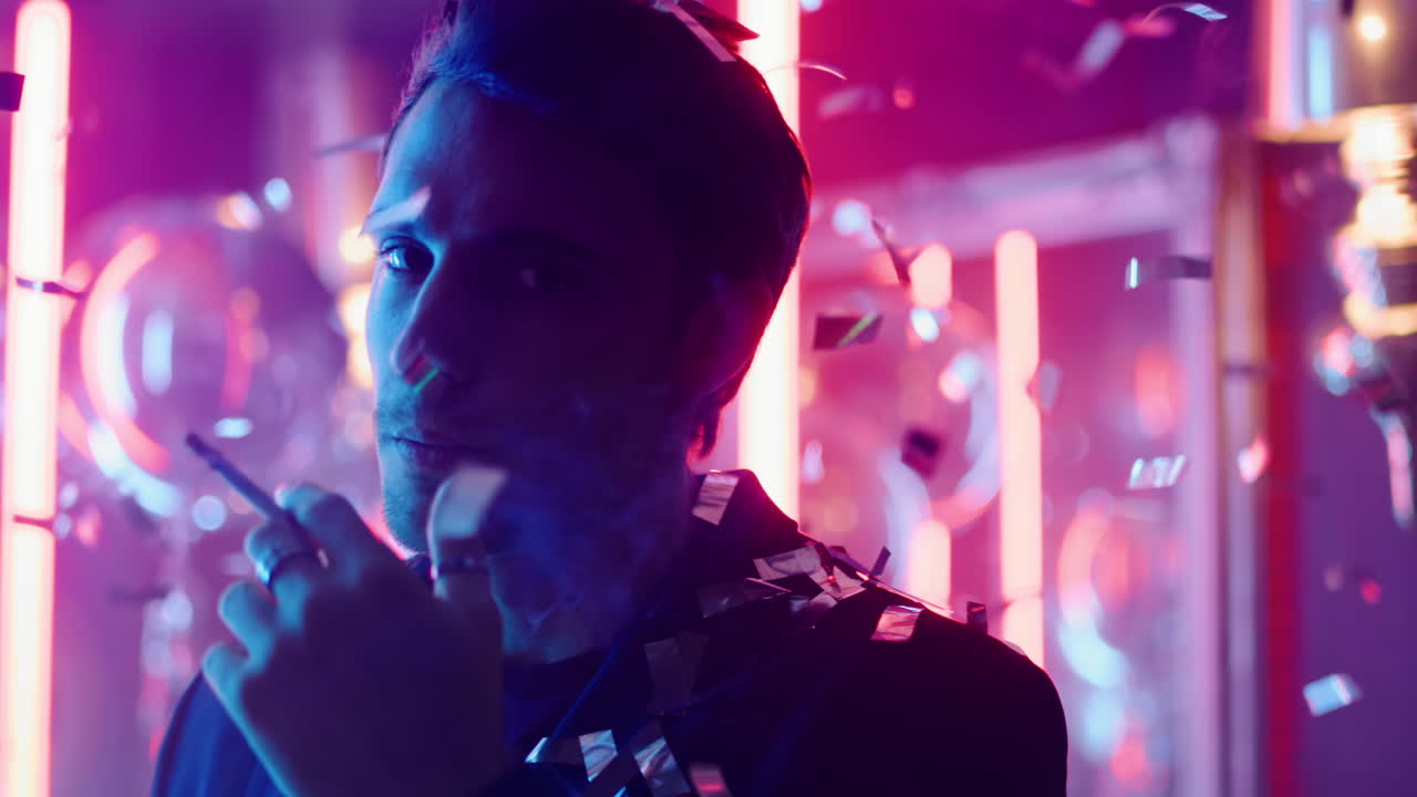 joven fumando bajo confeti en una fiesta. tipo soplando humo en un club nocturno