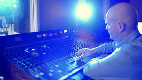 a male sound engineer siting at a mixer. the man is an audio technician in a professional recording studio operating a mixing desk