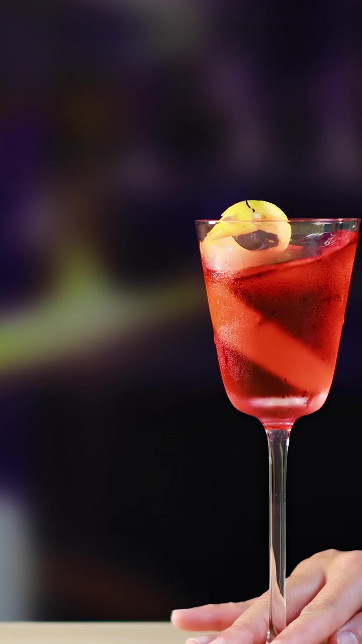 Una mano presenta elegantemente un cóctel Negroni contra un fondo vibrante y desenfocado. La escena está bien iluminada con un enfoque en la bebida