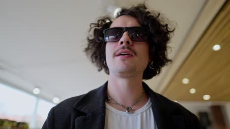 A-confident-and-cool-guy-with-curly-hair-and-black-sunglasses-walks-through-a-supermarket-and-looks-at-the-goods-with-his-eyes