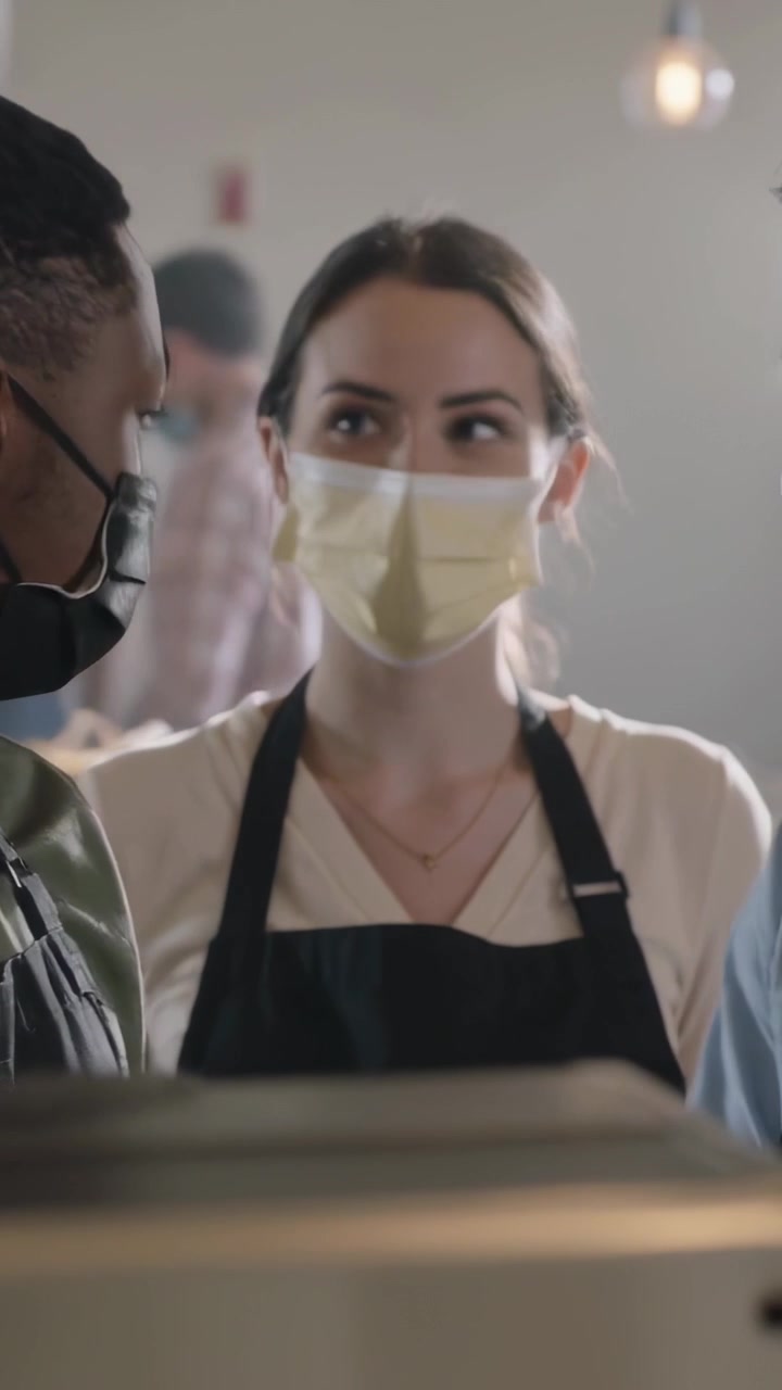 Vertical video: Pulling espresso for orders, barista wearing mask and apron at cafe counter