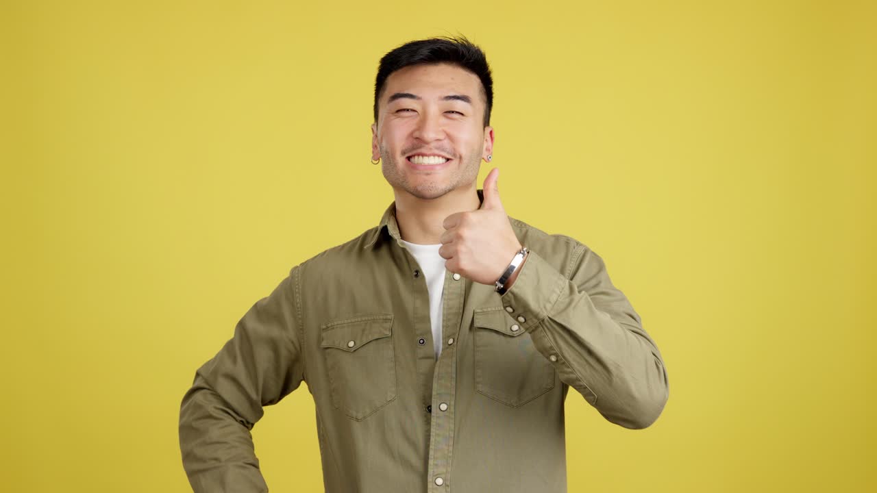 Happy Asian man giving a thumbs up on a yellow background