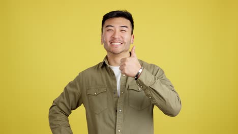 happy asian man giving a thumbs up on a yellow background