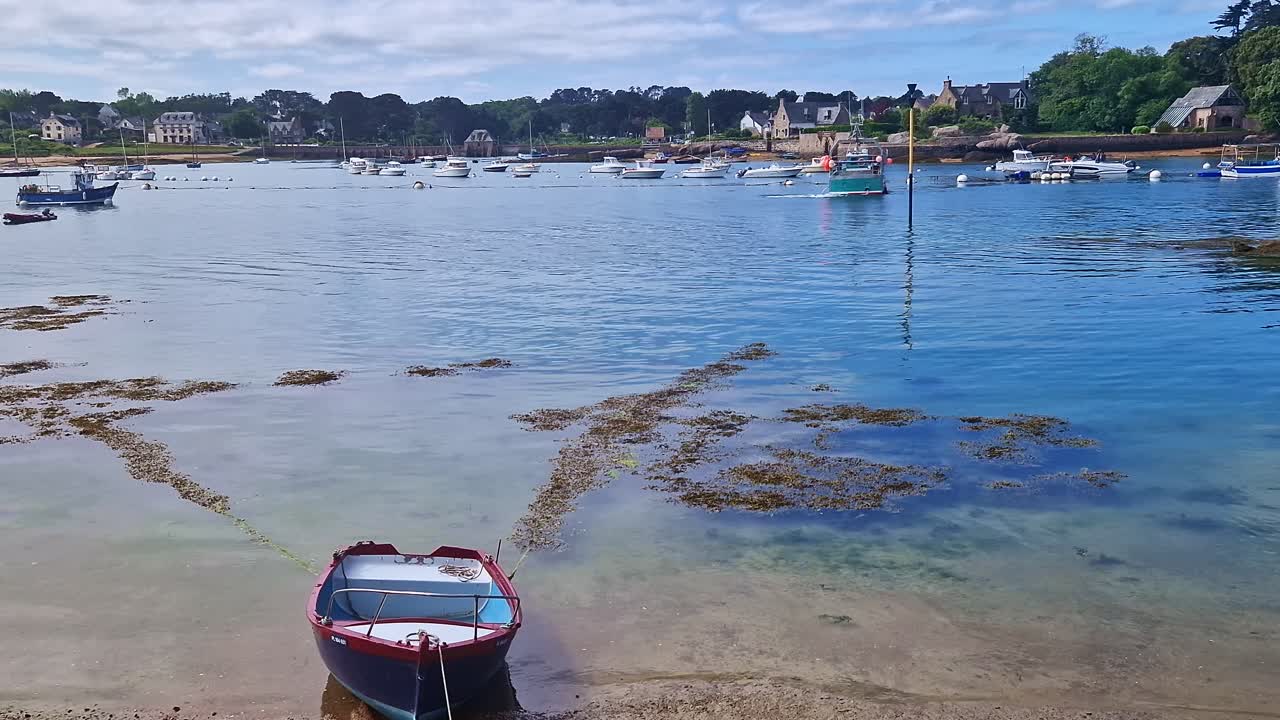Static shot of a moored boat at low tide in Perros-Guirec, with town and trees in the distance