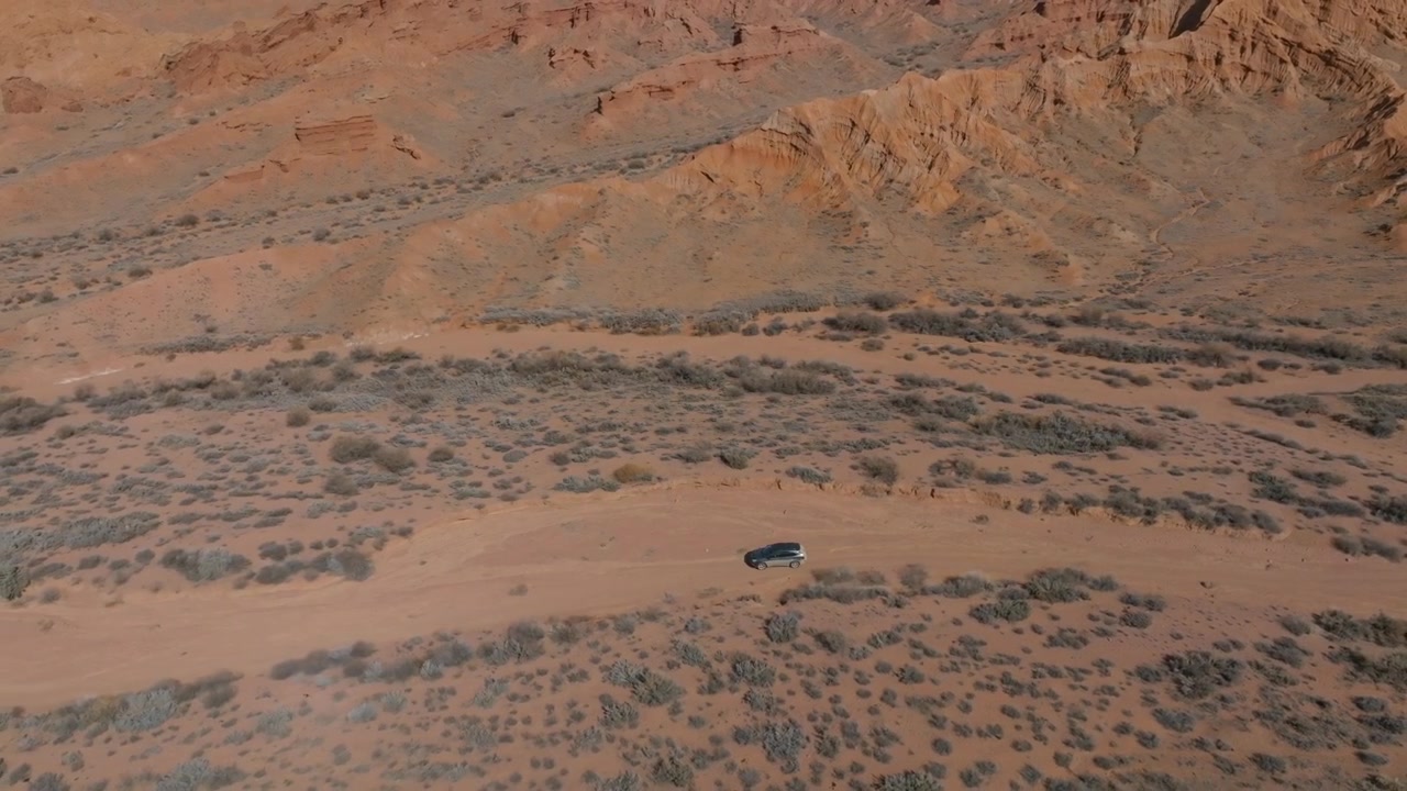 Filmato drone di colline rocciose di arenaria rossa e un paesaggio di canyon arido con un SUV che percorre una pista polverosa nel Canyon di Marte, Regione di Issyk-Kul, Kirghizistan
