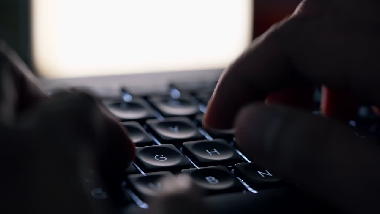 Close up footage of young businessman hands busy working, searching and studying by typing on glowing keyboard in the dark for send emails and surf on a web browser, dutch angle shot