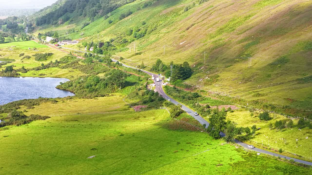 Aerial view of winding rural road, green hills, lake, and valley in bright daylight