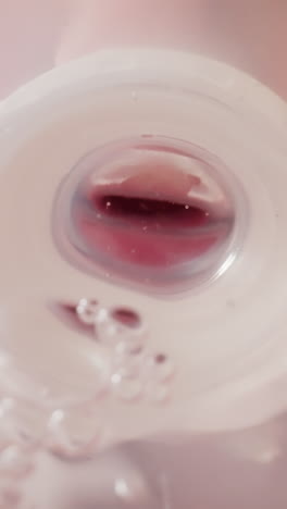 toddler holds baby bottle with clear water and drinks liquid using silicone pacifier. oxygen bubbles sway in drinking container macro low angle shot