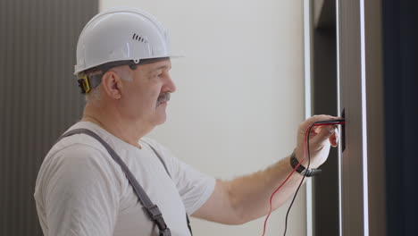 electrician checks the operation of the wall control unit for lamps and illumination of walls and ceiling with a modern house system after installation and repair