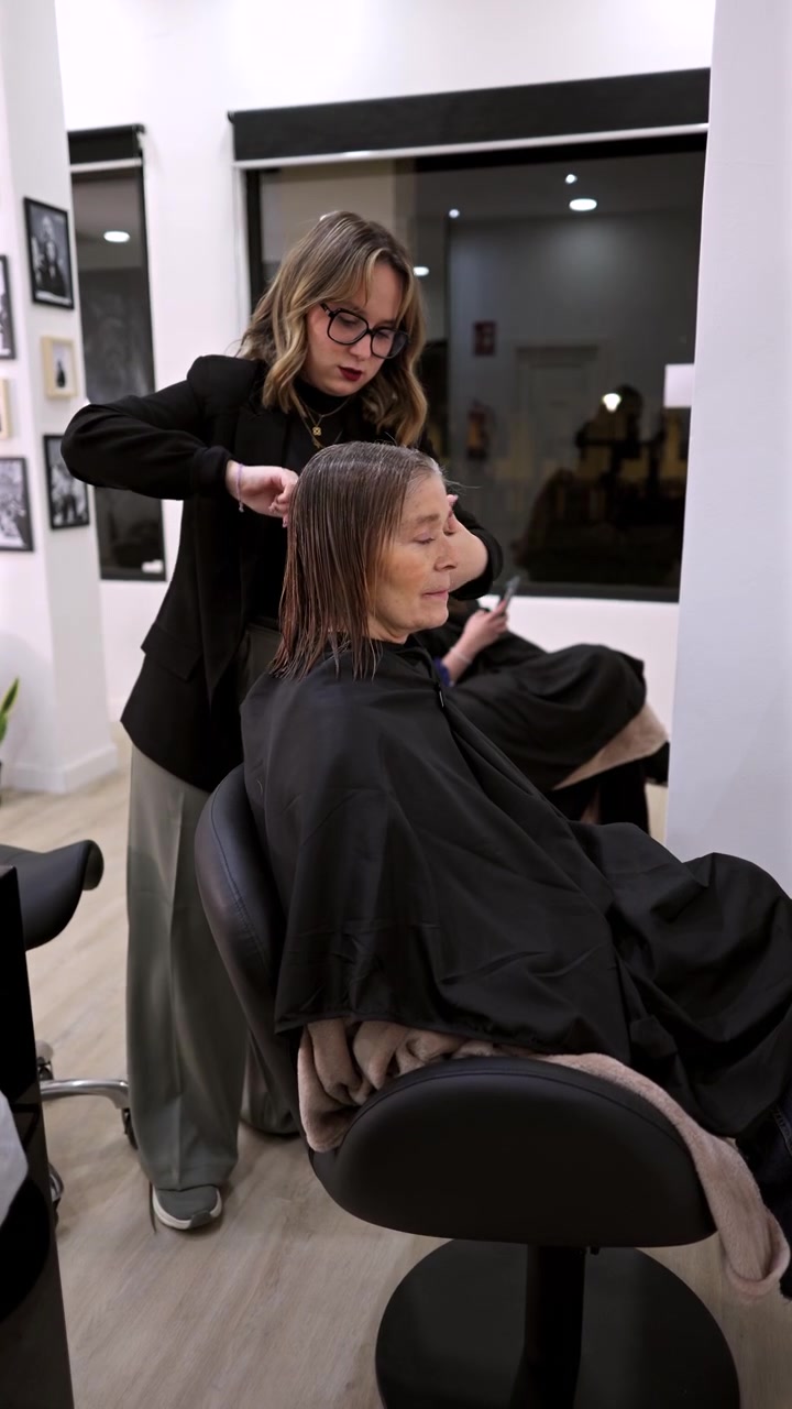Parrucchiere professionista che pettina e taglia i capelli a una donna matura in salone