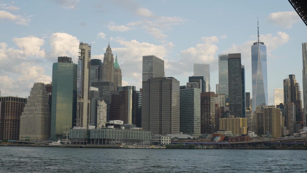 Toma panorámica amplia cinematográfica en cámara lenta del horizonte de la ciudad de Nueva York, con el Puente de Brooklyn, el East River y los icónicos rascacielos de Manhattan.