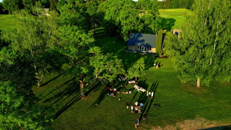 Toma-Aérea-De-Turistas-Disfrutando-De-Un-Picnic-En-Un-Prado-Con-Una-Cabaña-De-Campo-En-Letonia