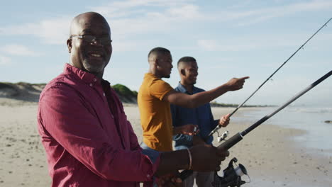 african american senior father and twin teenage sons standing on a beach fishing and talking