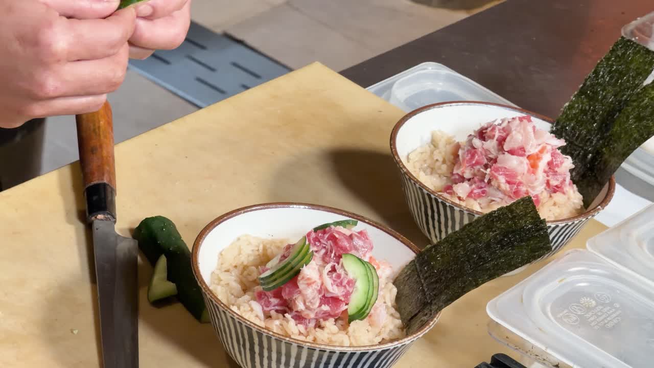 Close-up of chef arranging cucumber on minced tuna rice bowl under bright kitchen lighting