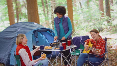 grupo de amigas en vacaciones de campamento en el bosque comiendo comida y cantando junto a la guitarra