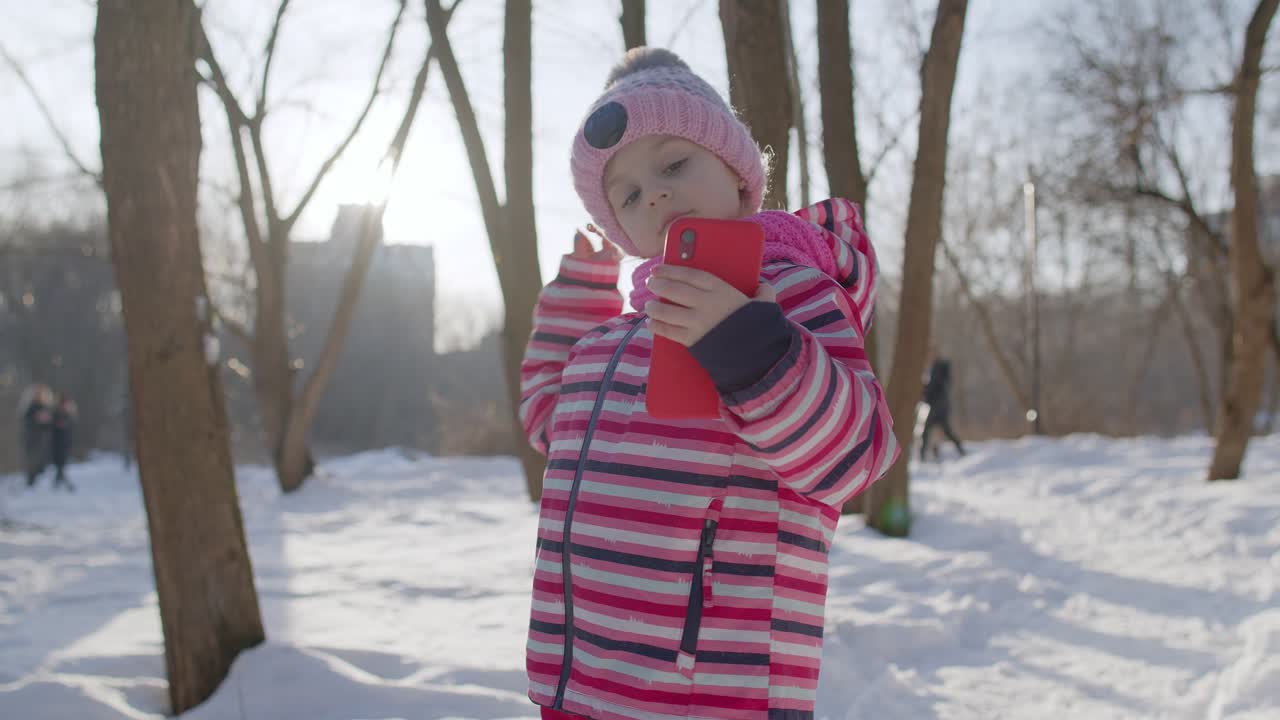 niña blogger haciendo llamada de video en teléfono móvil, foto selfie para redes sociales en el parque de invierno